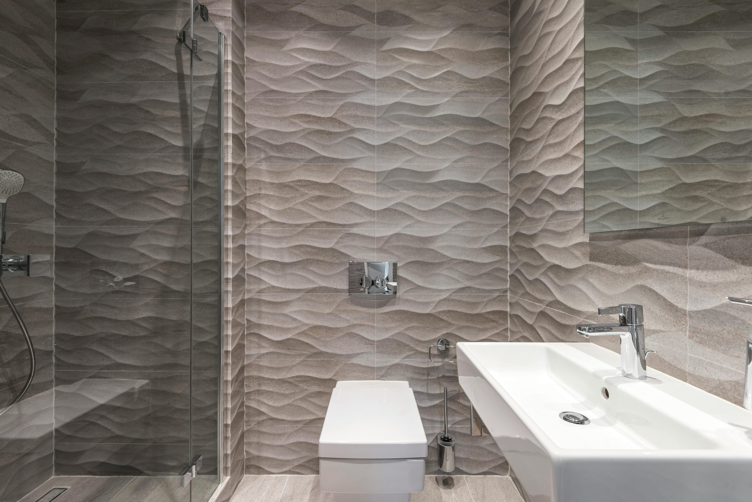 Sleek bathroom featuring textured walls, a glass shower, and a modern sink.