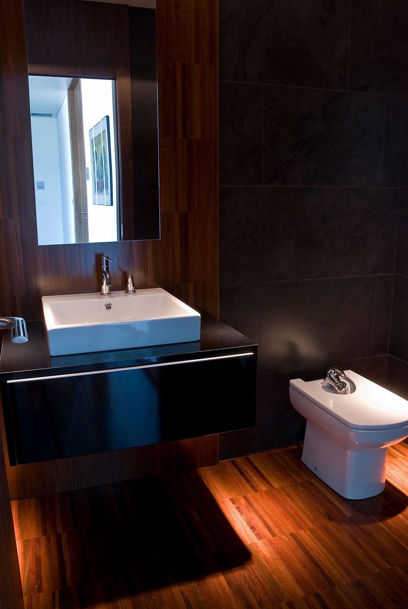 Sleek modern bathroom interior featuring a bidet, sink, and mirror with wood paneling.