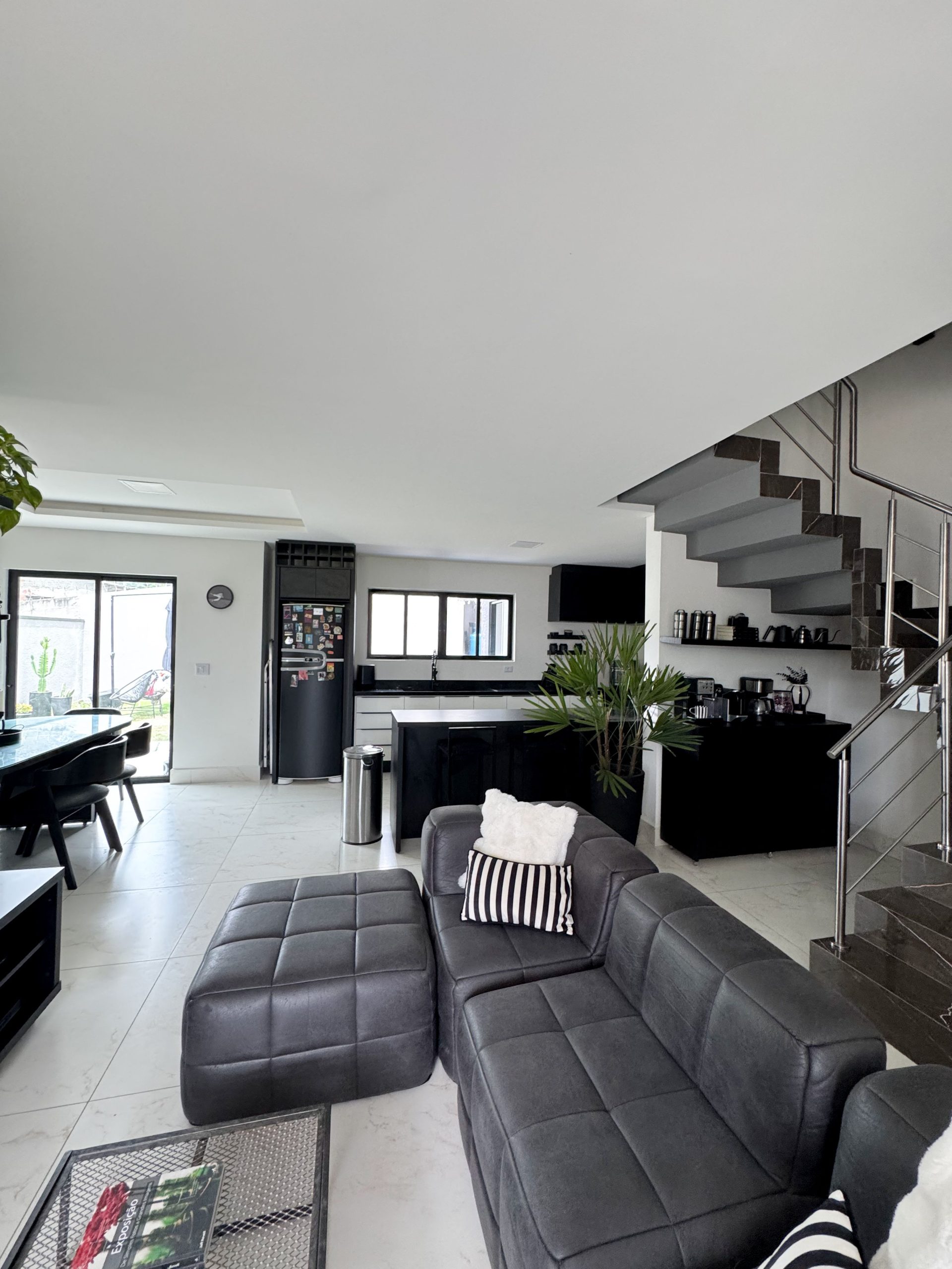 Sleek modern interior with black sofa, kitchen, and staircase in a well-lit living space.