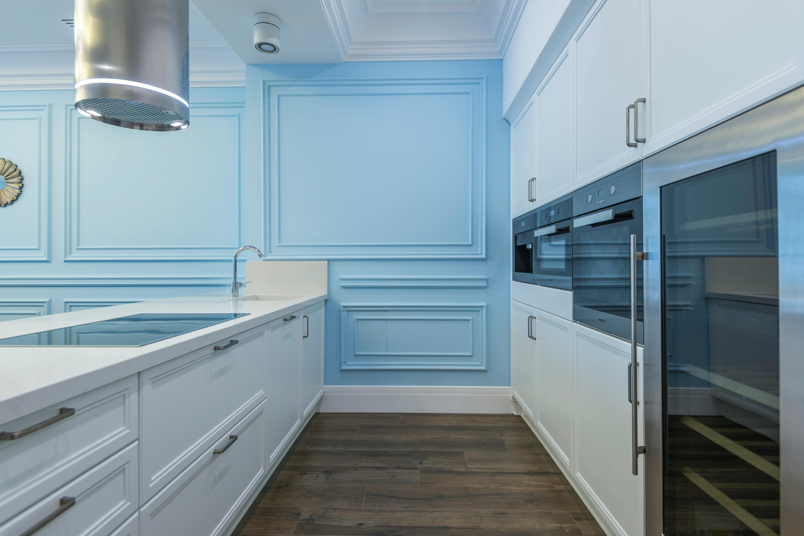 Sleek modern kitchen featuring white cabinetry, blue accent wall, and stainless appliances.