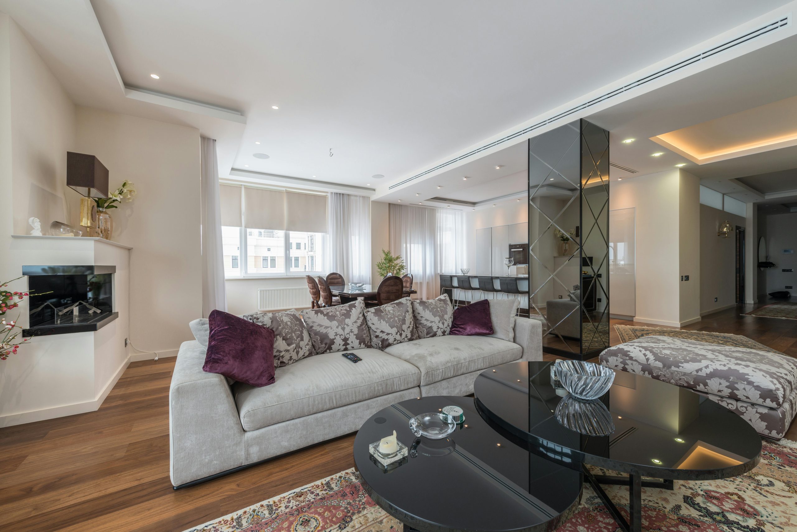 Small glass black table placed on carpet near sofa with pillows in spacious light living room in apartment in daytime