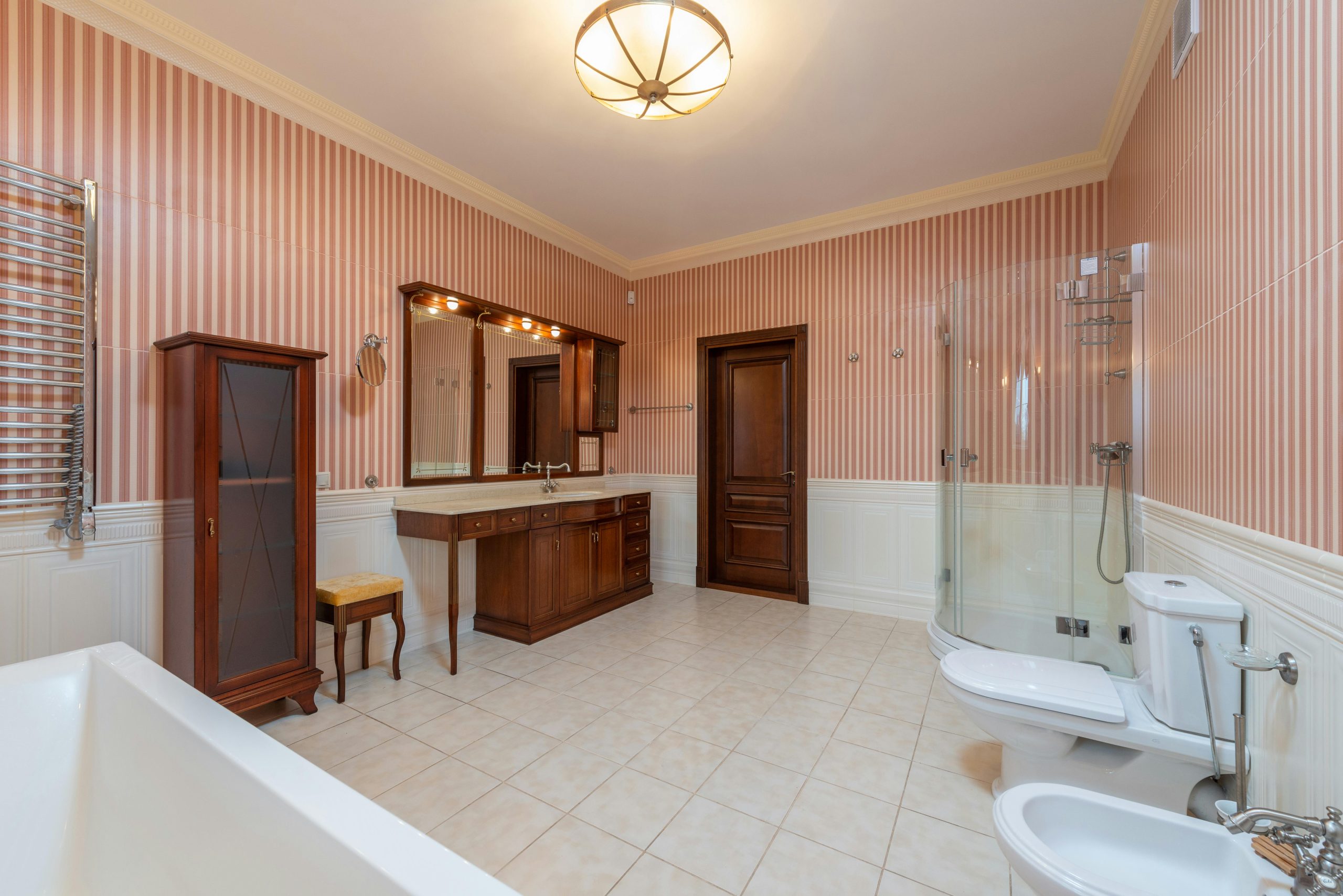 Spacious bathroom with vintage decor, featuring striped wallpaper and wooden furniture.