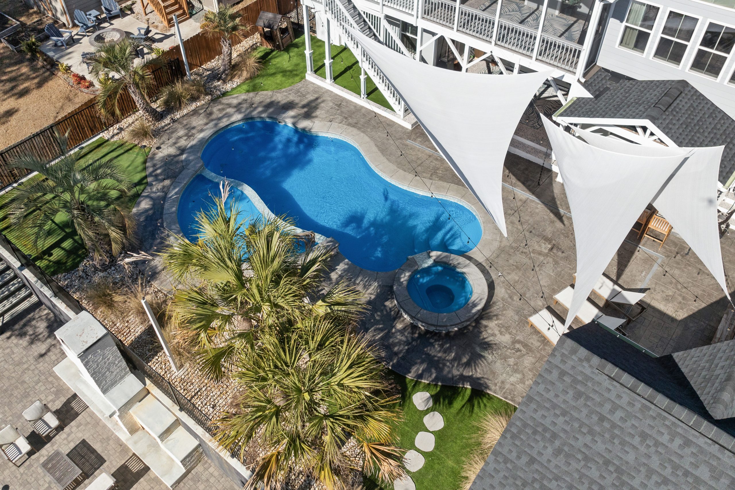 Stunning aerial view of a modern backyard featuring a blue swimming pool, palm trees, and stylish shade sails.