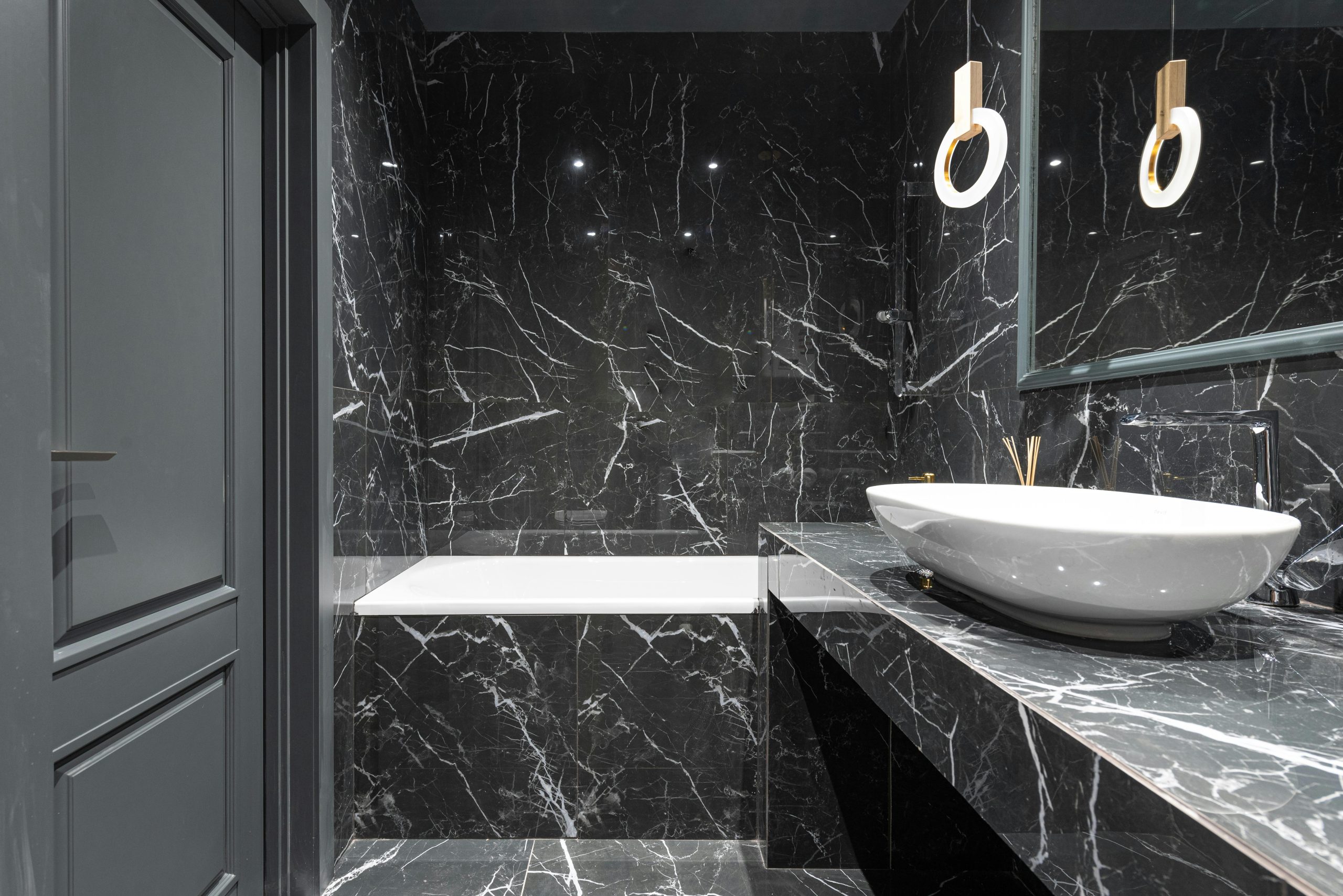 Stylish bathroom with bathtub and round lamp hanging above sink placed on marble surface