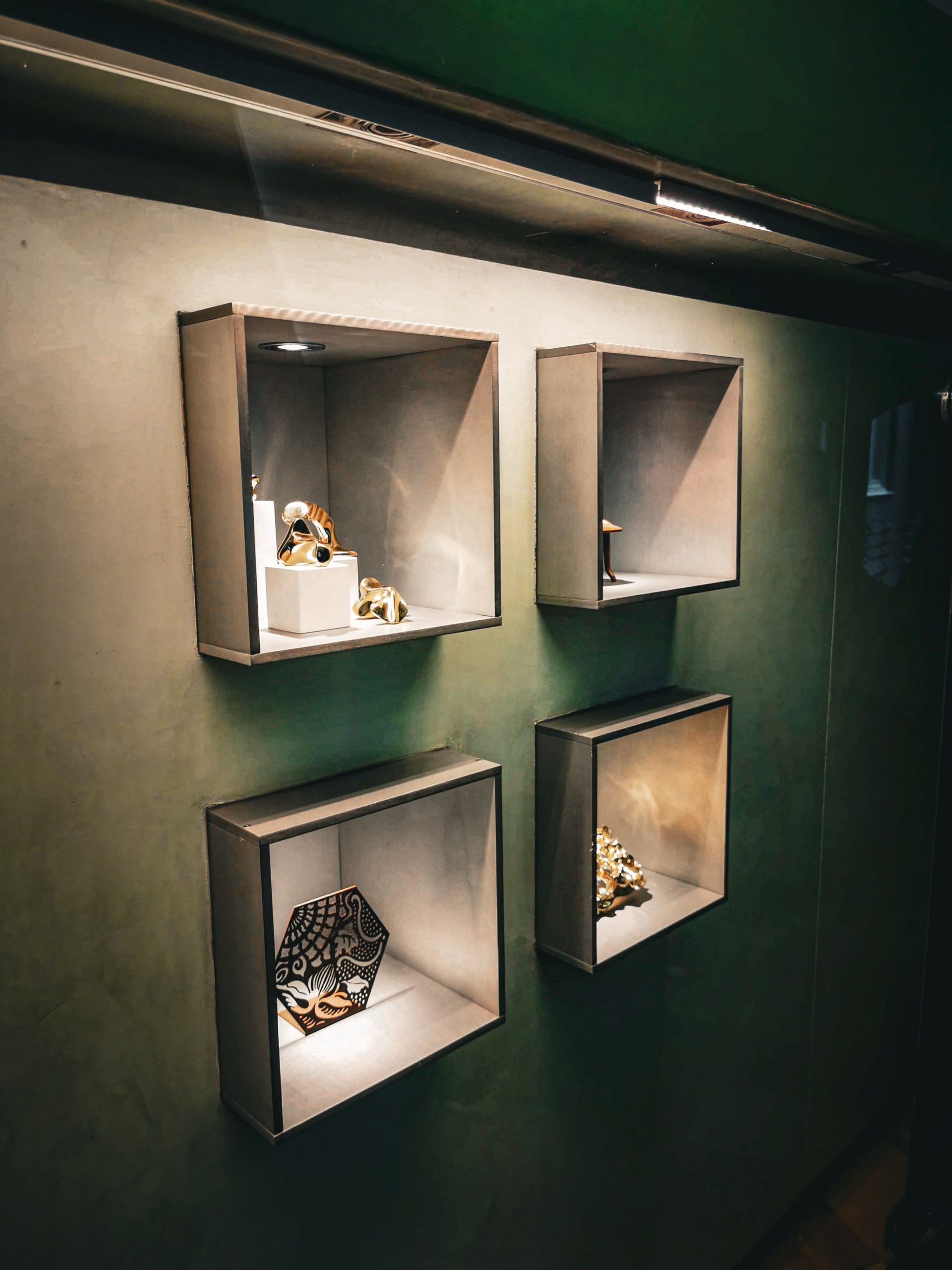 Stylish modern art exhibits showcased in lighted, minimalist display boxes against a dimly lit wall.