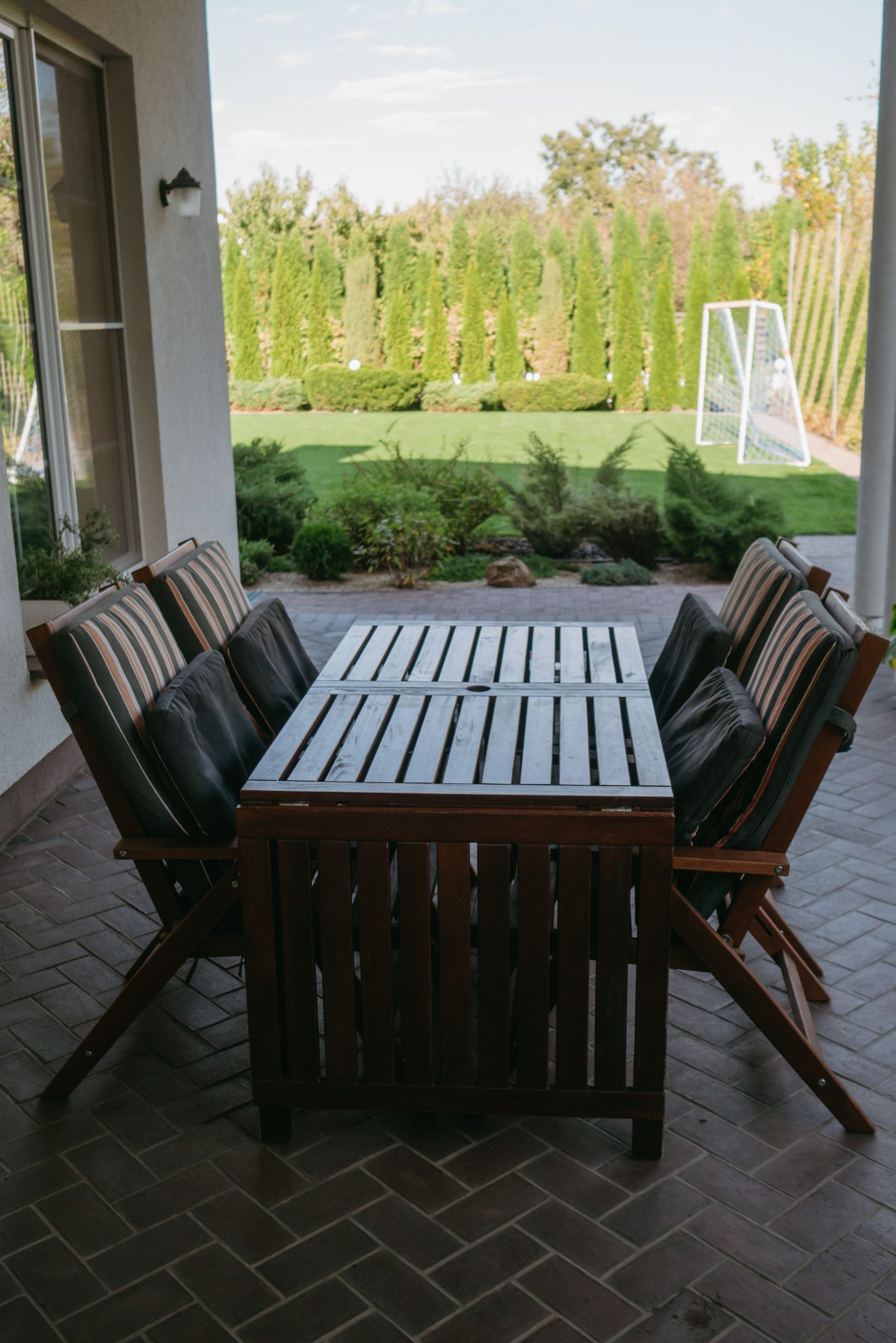 Stylish patio setup with wooden furniture and lush greenery in a sunny backyard.