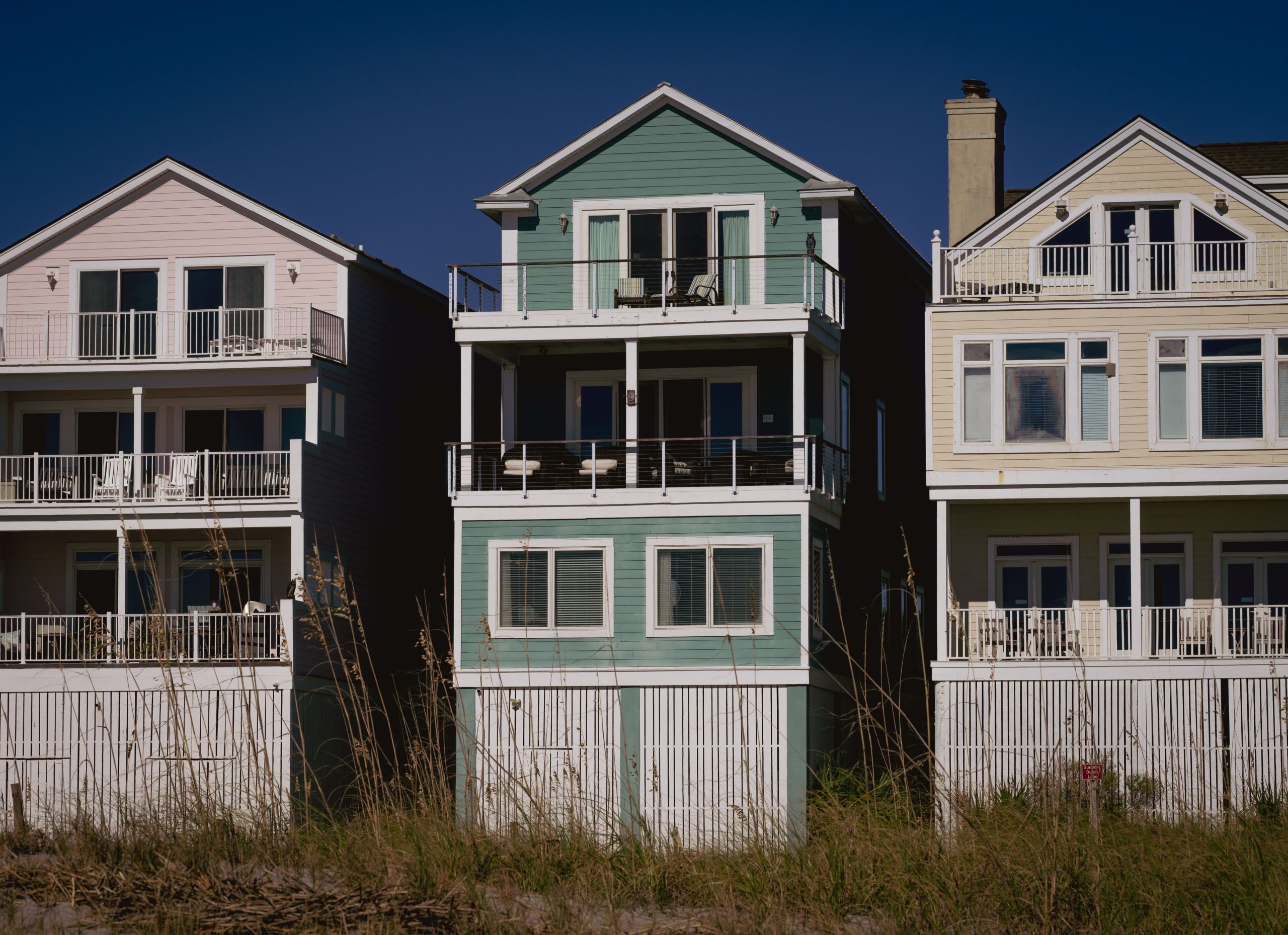 Sunny day view of colorful coastal homes with wooden siding and balconies, perfect for summer living.
