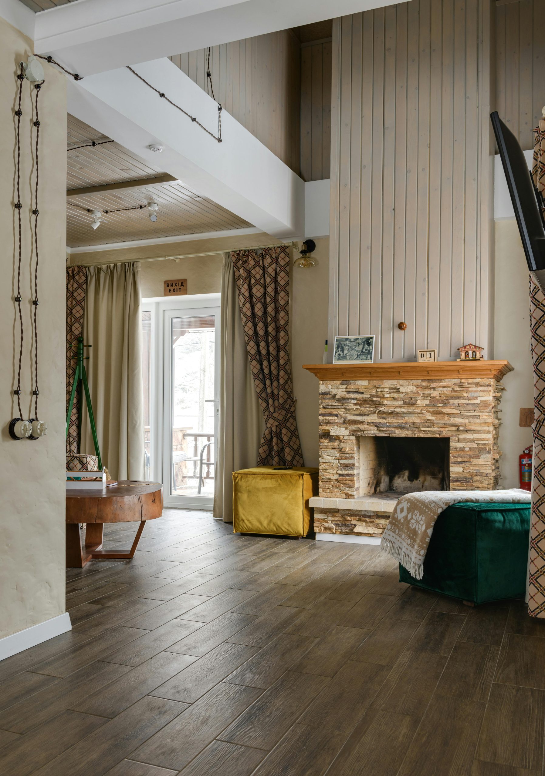 Warm and inviting living room interior with stone fireplace, wooden table, and elegant curtains.
