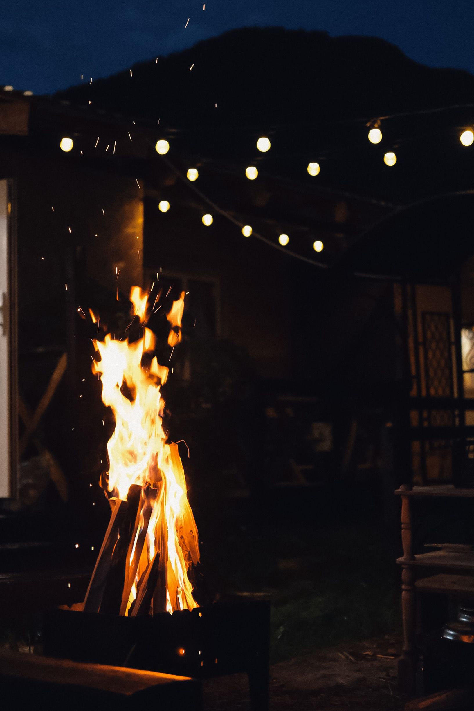 Warm bonfire glowing under string lights, perfect for a cozy night outdoors.
