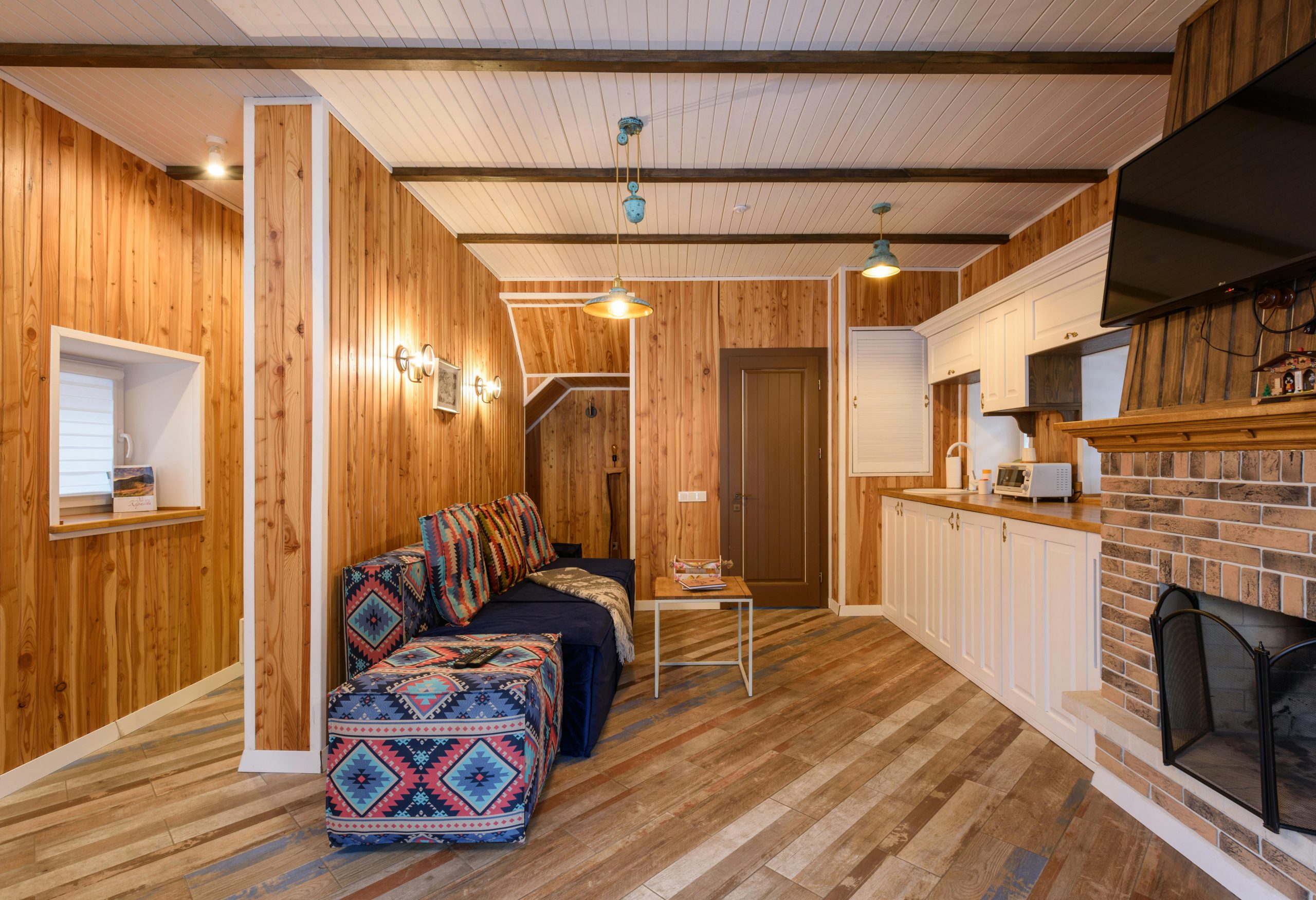 Warm rustic living room with wooden walls, modern kitchen, and a cozy fireplace.