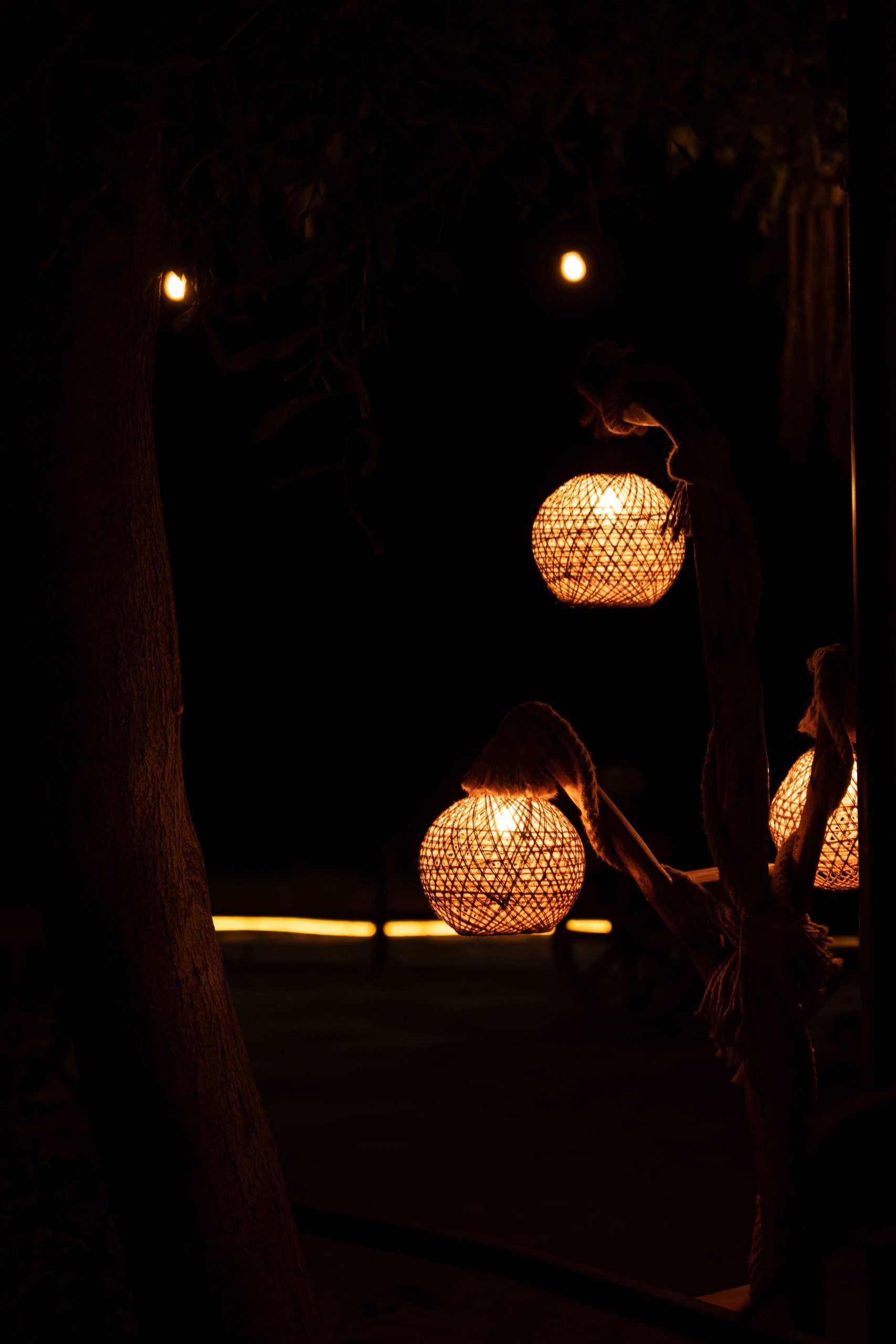 Warmly illuminated lanterns hanging in a park at dusk, creating a cozy atmosphere.