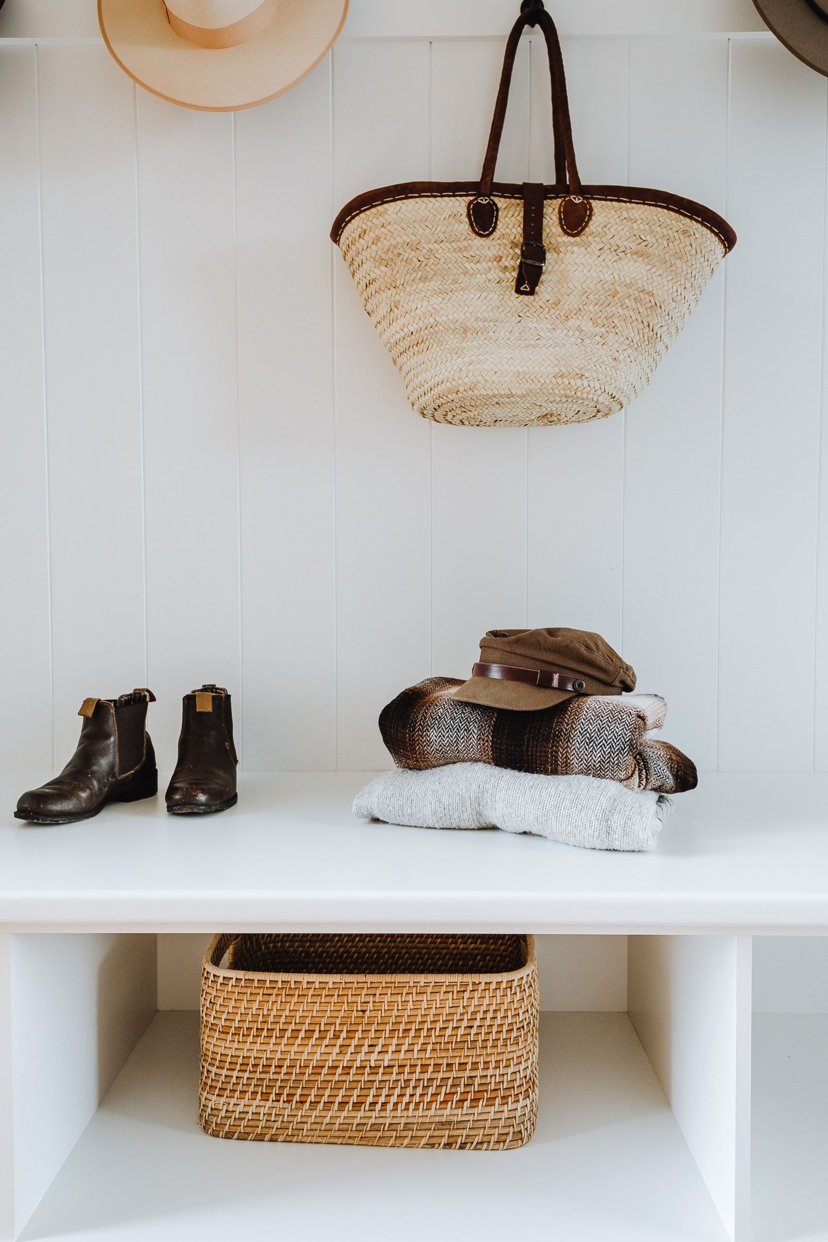 White hallway bench with wicker basket and bag and stylish boots with hats and plaids