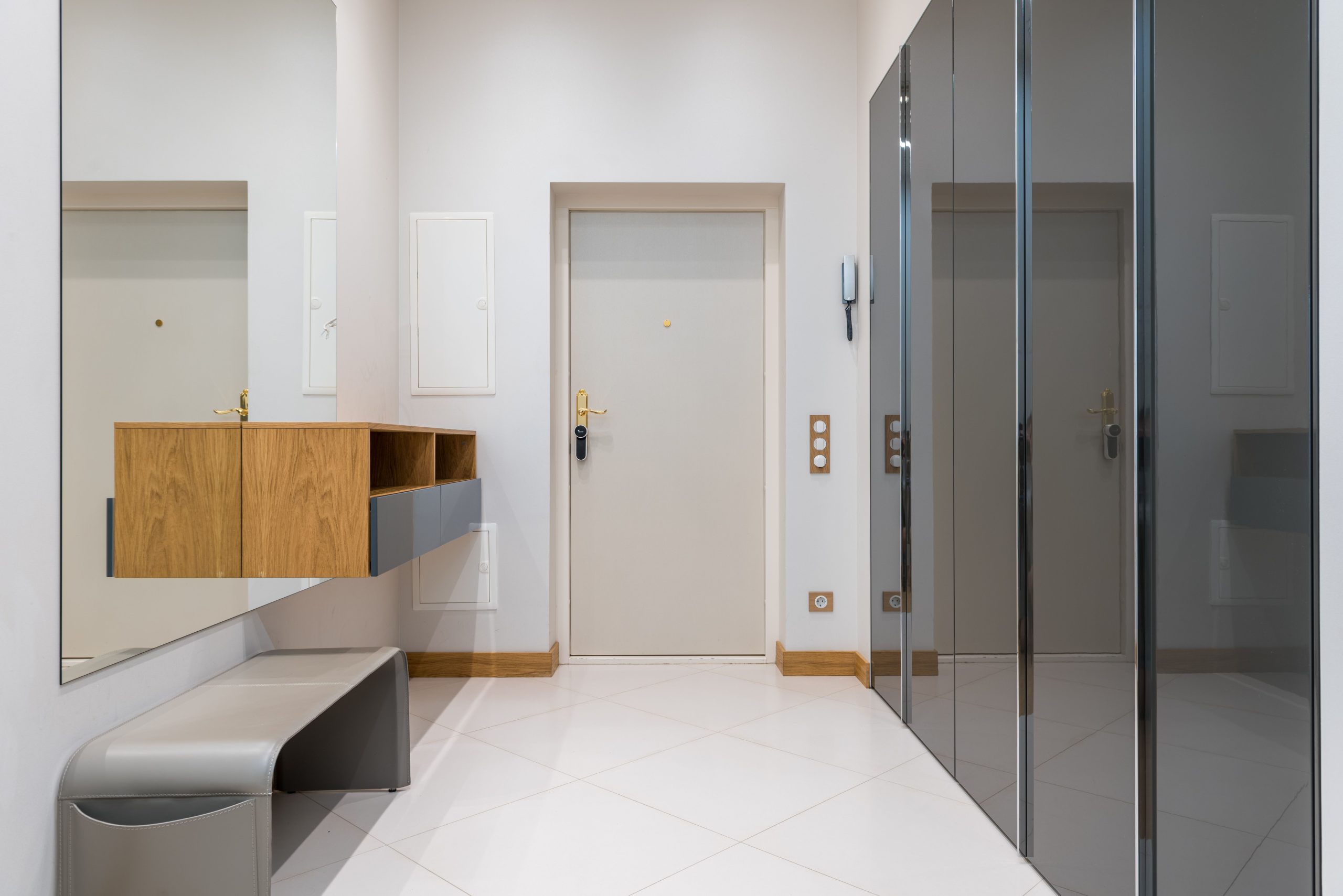 Wooden shelf with bench placed in front of wardrobe with mirrored doors in corridor of modern apartment